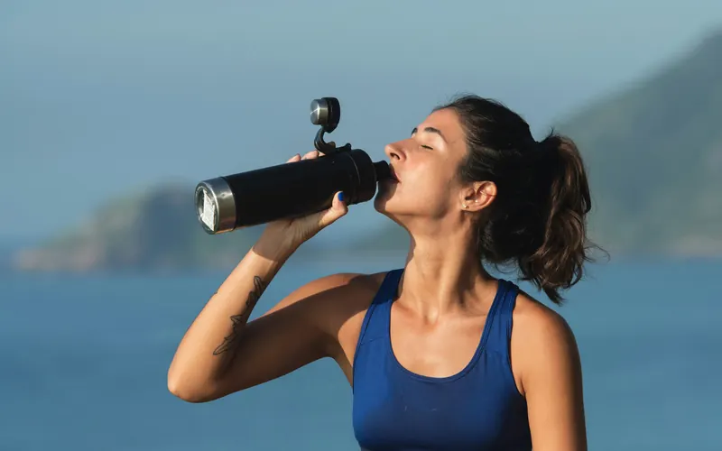 Woman drinking from a water bottle by the sea