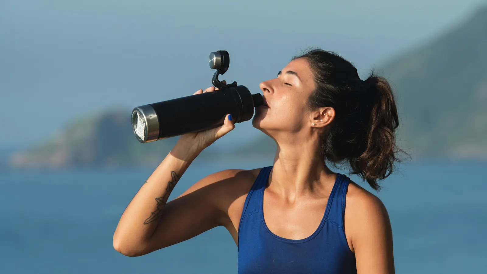Woman drinking from a water bottle by the sea